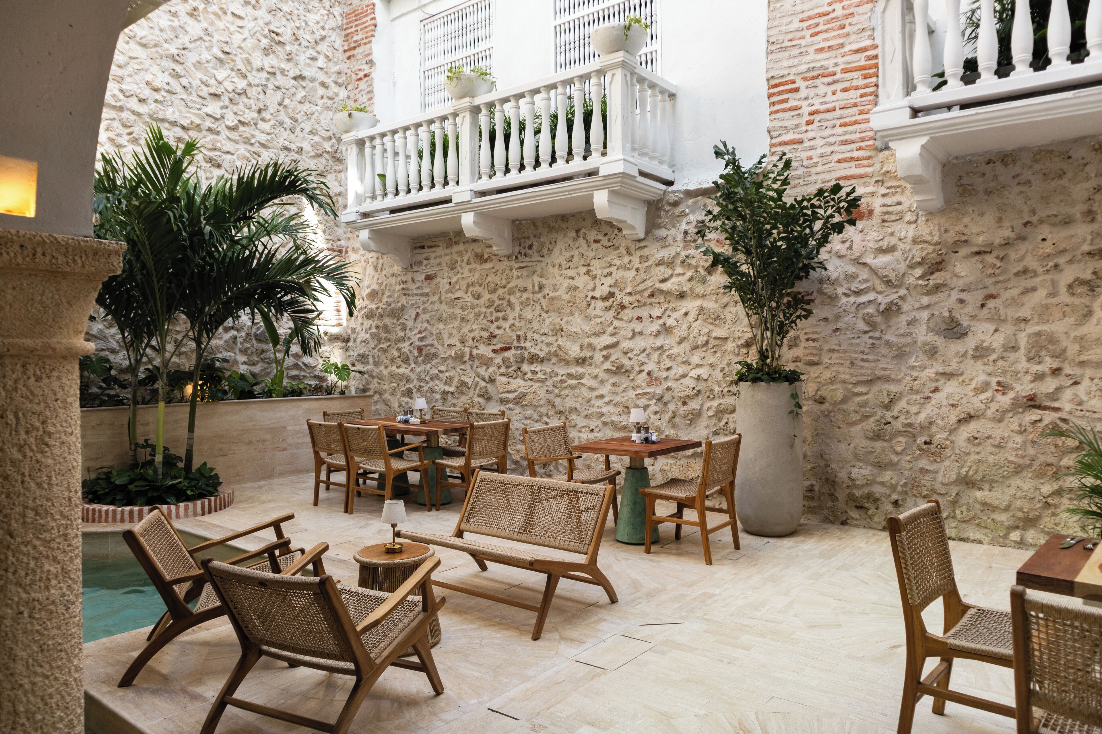 Un patio al aire libre con mobiliario de mimbre, un muro de piedra y una piscina pequeña.