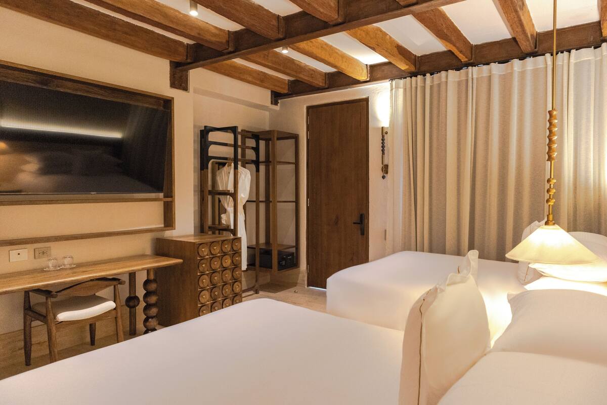 Habitació d'hotel amb dos llits, una taula de treball amb cadira, un armari, un mirall i una porta que dóna a una altra habitació.