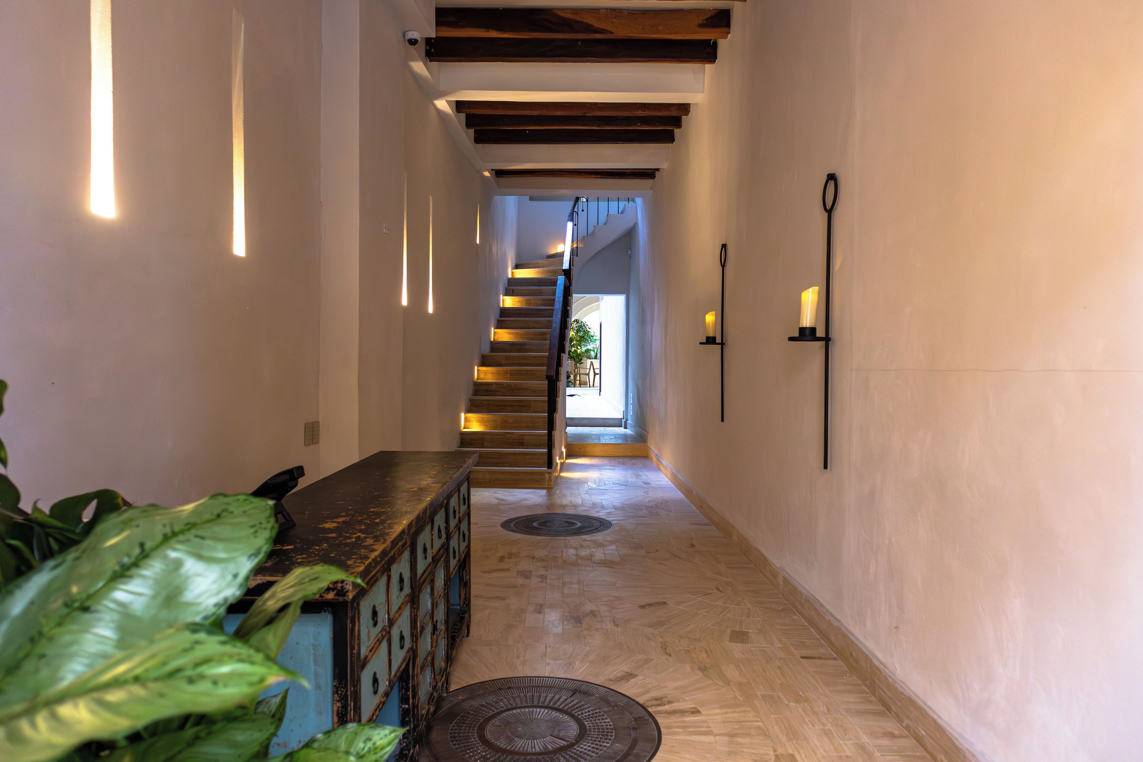 Un pasillo con una escalera de madera, un banco y una lámpara fijada a la pared.