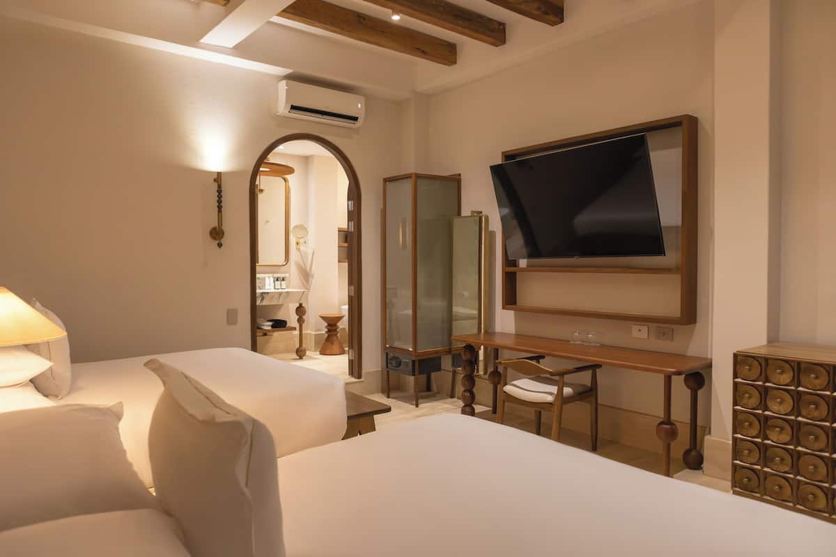 Una habitació d'hotel amb dos llits, un escriptori, una cadira, un mirall i una televisió.