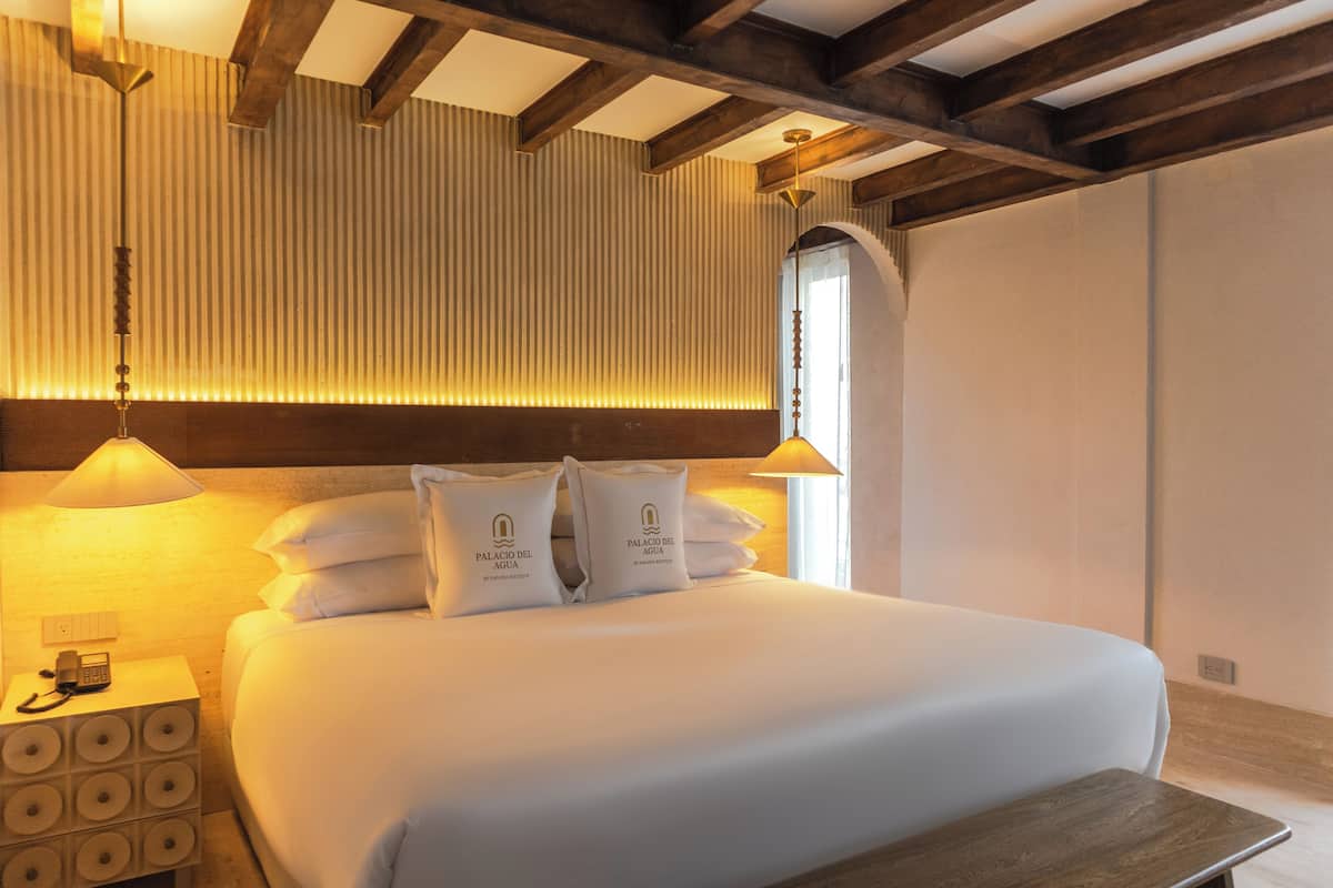 Habitació d'hotel amb un llit gran, una taula de nit amb una làmpada i un panell de fusta al capçal.