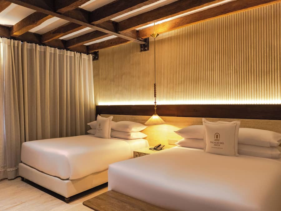 A hotel room with two beds, a nightstand, a lamp, and a curtain.