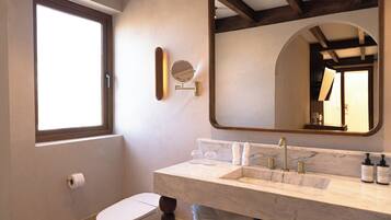 A bathroom with a toilet, a sink with a marble countertop, a large mirror, and a window.