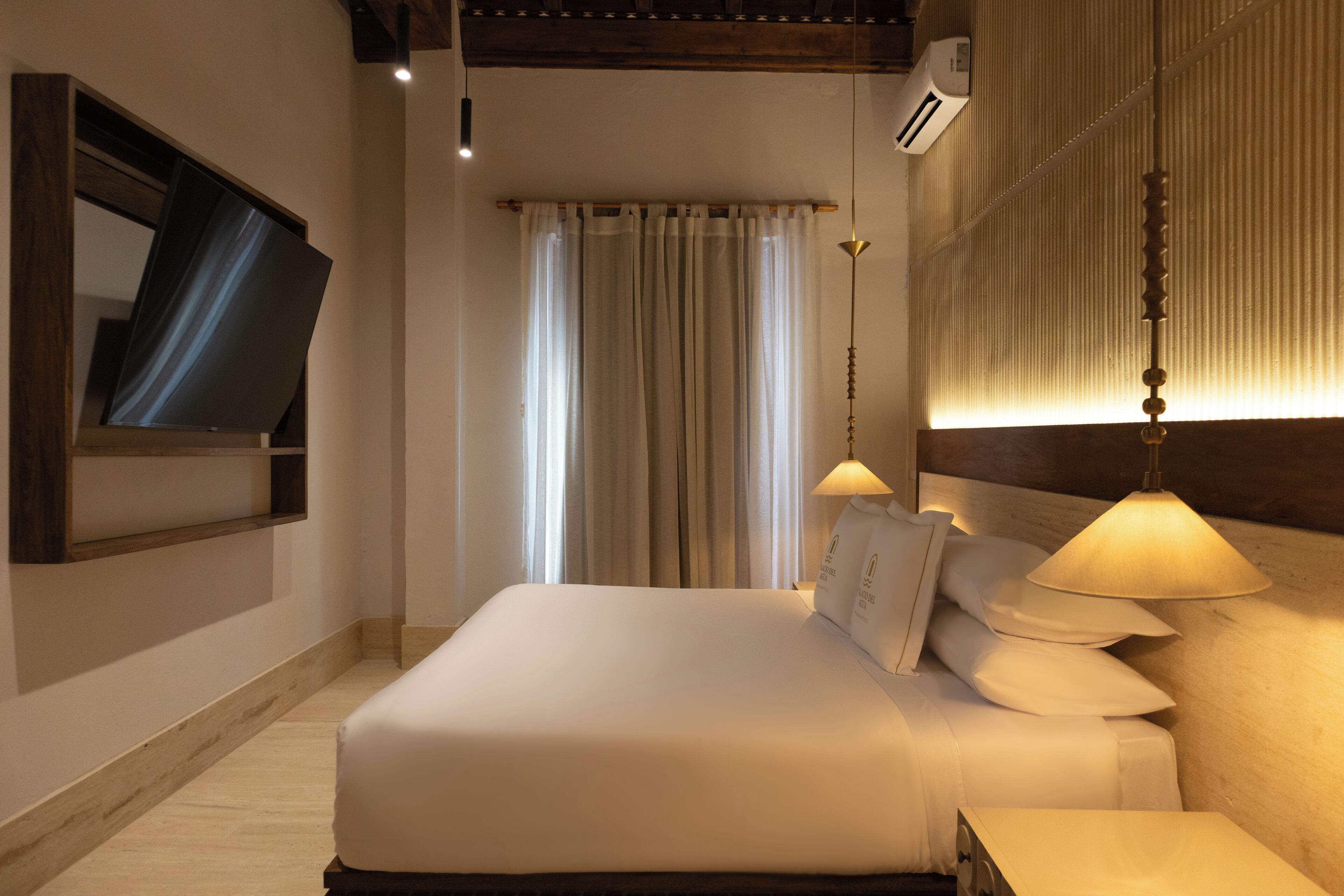 A neatly made bed with white linens, a bedside lamp, and a wall-mounted TV.