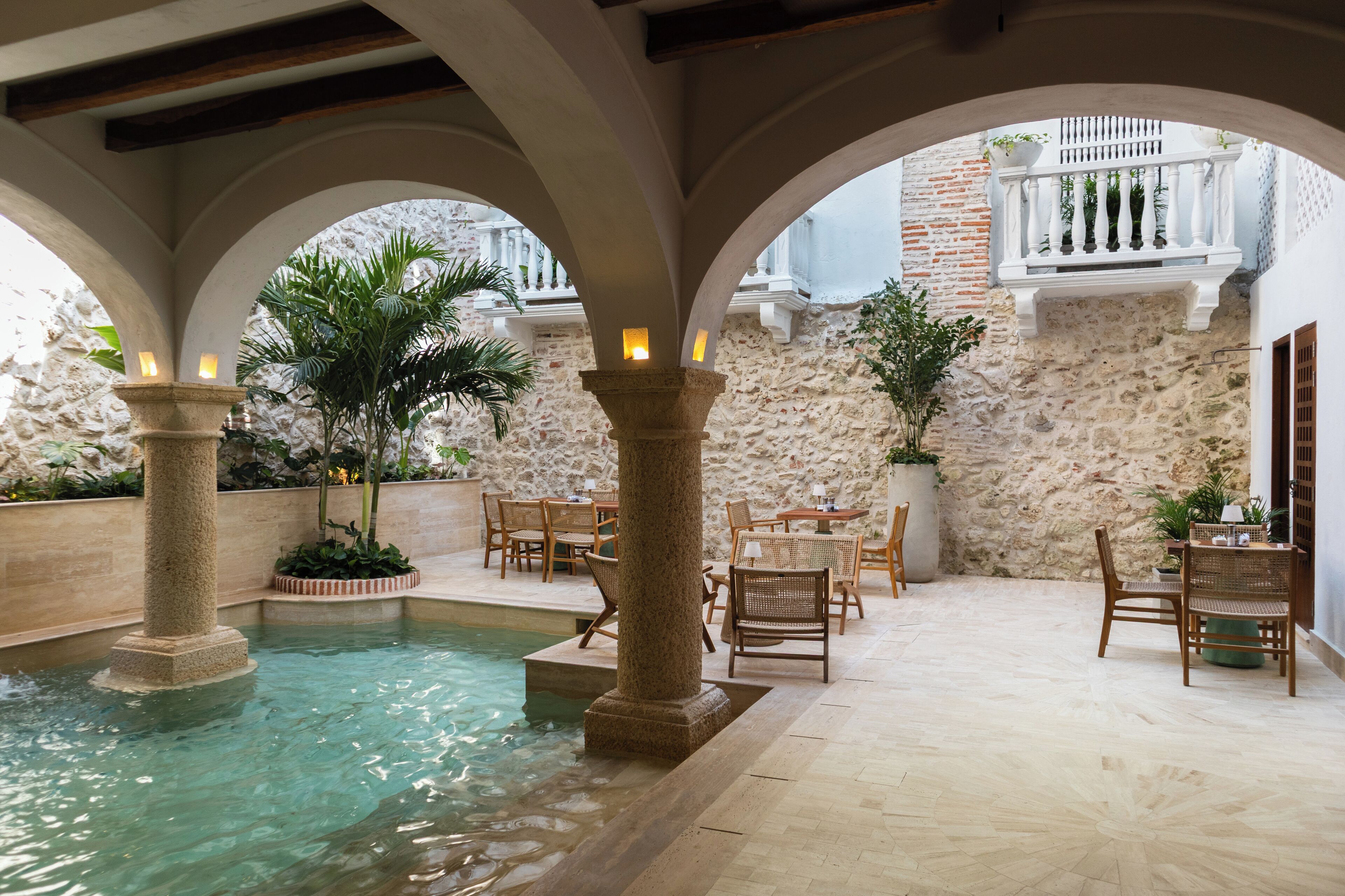 Un espace piscine agrémenté de colonnes, de tables et de chaises en pierre, entouré de murs en pierre et doté d’un balcon.