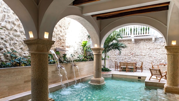 Zona de piscina con columnas de piedra, fuentes de agua y mobiliario exterior.