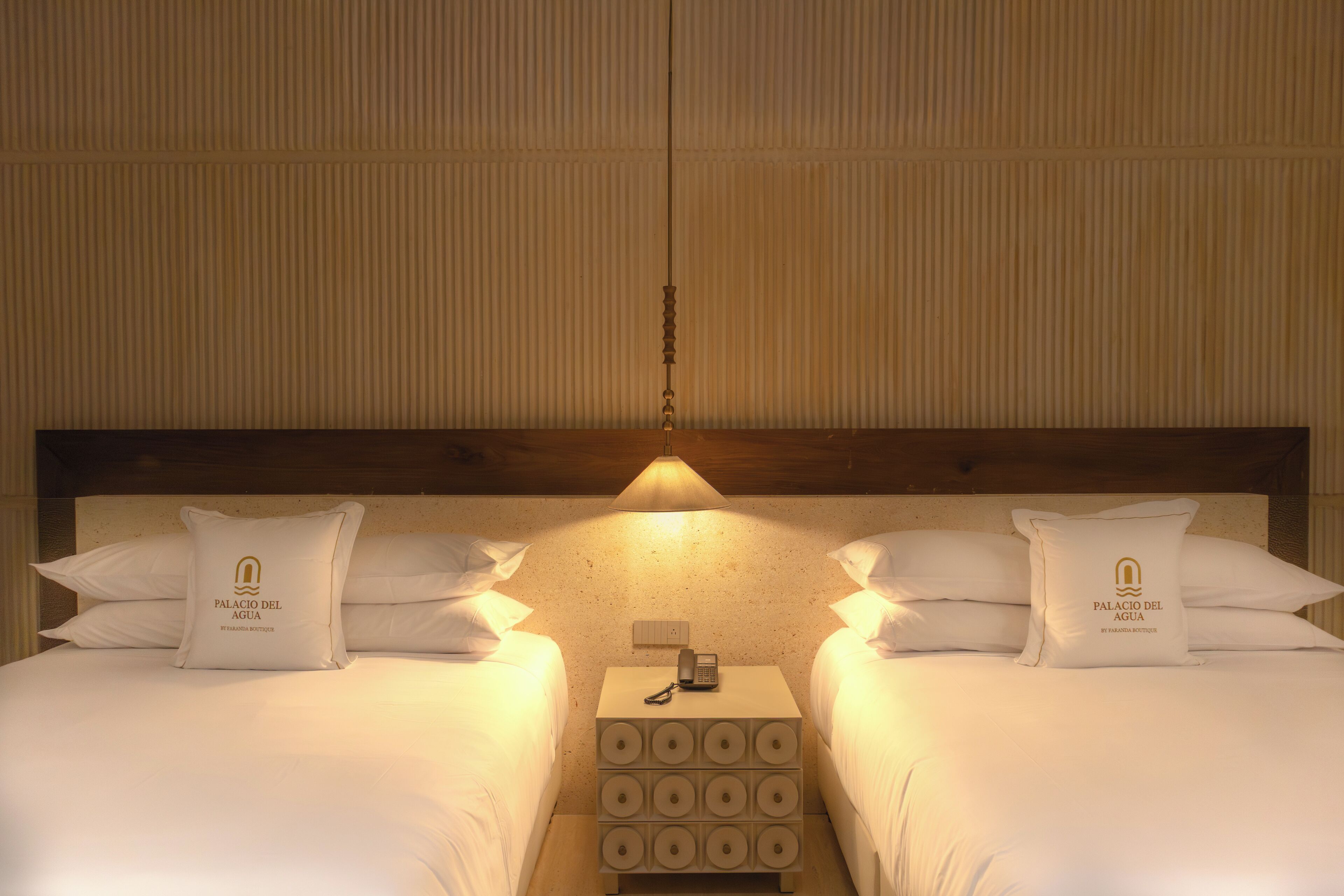 Ein Hotelzimmer mit zwei Betten, einem Nachttisch mit Telefon und einer Wandlampe.
