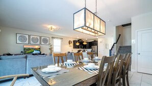 A dining area with a wooden table set for six, surrounded by wooden chairs. A hanging light fixture above the table provides illumination. - ChampionsGate Resort 8BR Home w/ Pool, Hot Tub, Theater, Game Room  & Much More! (Kissimmee)