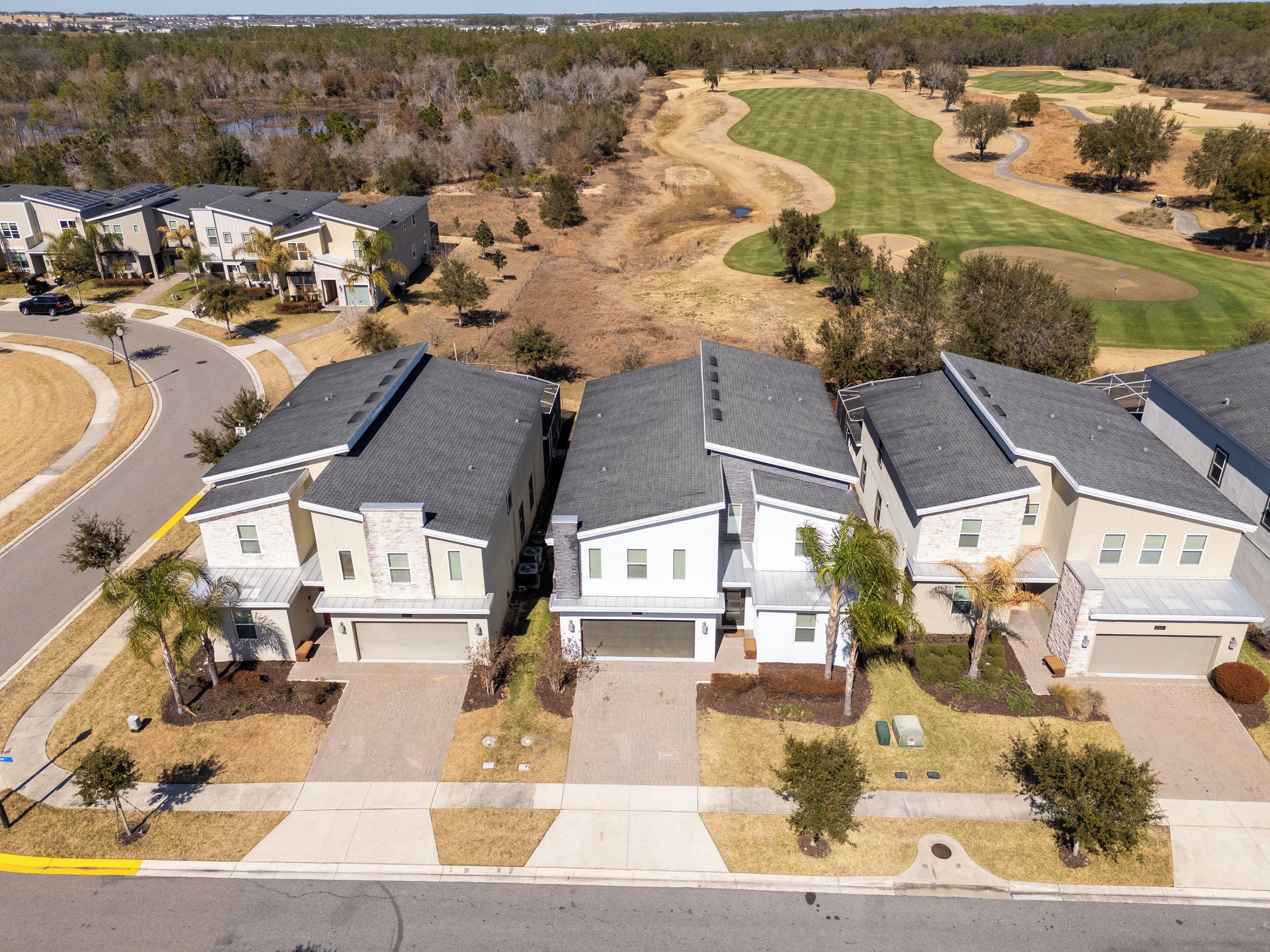 A residential area with modern houses, a golf course, and a road.