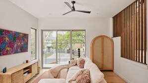 Ein modernes Wohnzimmer mit einer Couch, einem Deckenventilator, einem Holzschrank und einem großen Fenster.