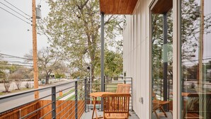 Ein Balkon mit einem Holztisch und Stühlen, ein blauer Stuhl, ein Holzzaun und Blick auf Bäume und eine Straße.