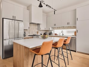 A modern kitchen with white cabinets, a stainless steel refrigerator, a wooden island with bar stools, and a hanging light fixture. - Modern East Austin Pool Home - Sleeps 8 - 8 Min DT (Austin)