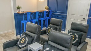 A room with four black leather chairs, each with a pillow featuring a 'B' emblem. A reception desk with blue chairs is in the background. - Spacious 5-Bedroom 6 Bed House In Gorgeous Upper Montclair with AC, Theater Room (Upper Montclair)