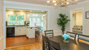 A dining area with a wooden table and chairs, a vase with flowers, and a view of the kitchen and living room. - Spacious 5-Bedroom 6 Bed House In Gorgeous Upper Montclair with AC, Theater Room (Upper Montclair)