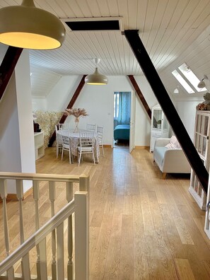 A spacious loft with a wooden floor, a dining area with a table and chairs, a sofa, and a staircase with a railing. - Charming 70-square-meter private home with a garden, located 5 bus stops from downtown Strasbourg   (Schiltigheim)