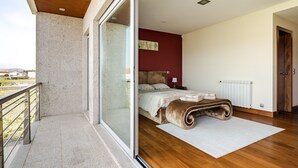 Une chambre dotée d’une grande porte-fenêtre coulissante donnant sur un balcon, d’un lit avec une tête de lit, d’un radiateur et d’un plancher en bois.