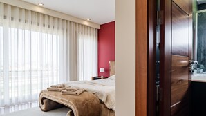 Ein modernes Schlafzimmer mit einem großen Bett, einem Holzschrank und Blick auf die Stadt durch das Fenster.