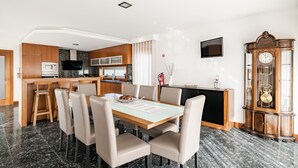 Eine moderne Küche mit Holzausstattung, einem Esstisch mit Stühlen, einem an der Wand montierten Fernseher und einer großen Holz-Wanduhren.