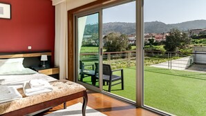 A bedroom with a large sliding glass door leading to a balcony with a view of a green lawn and distant buildings. - Casa Do Chino - Suite with Pool View (Belinho)