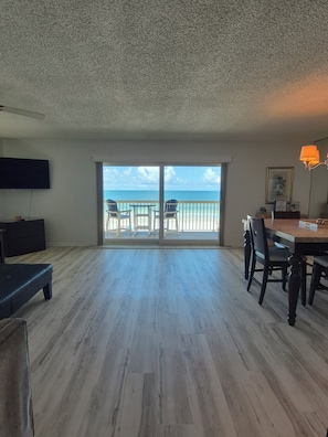 A spacious living area with a balcony overlooking the ocean, a flat-screen TV, and a dining table with chairs. - NEW UPGRADES on lovely Indian Rocks Beach (Indian Rocks Beach)