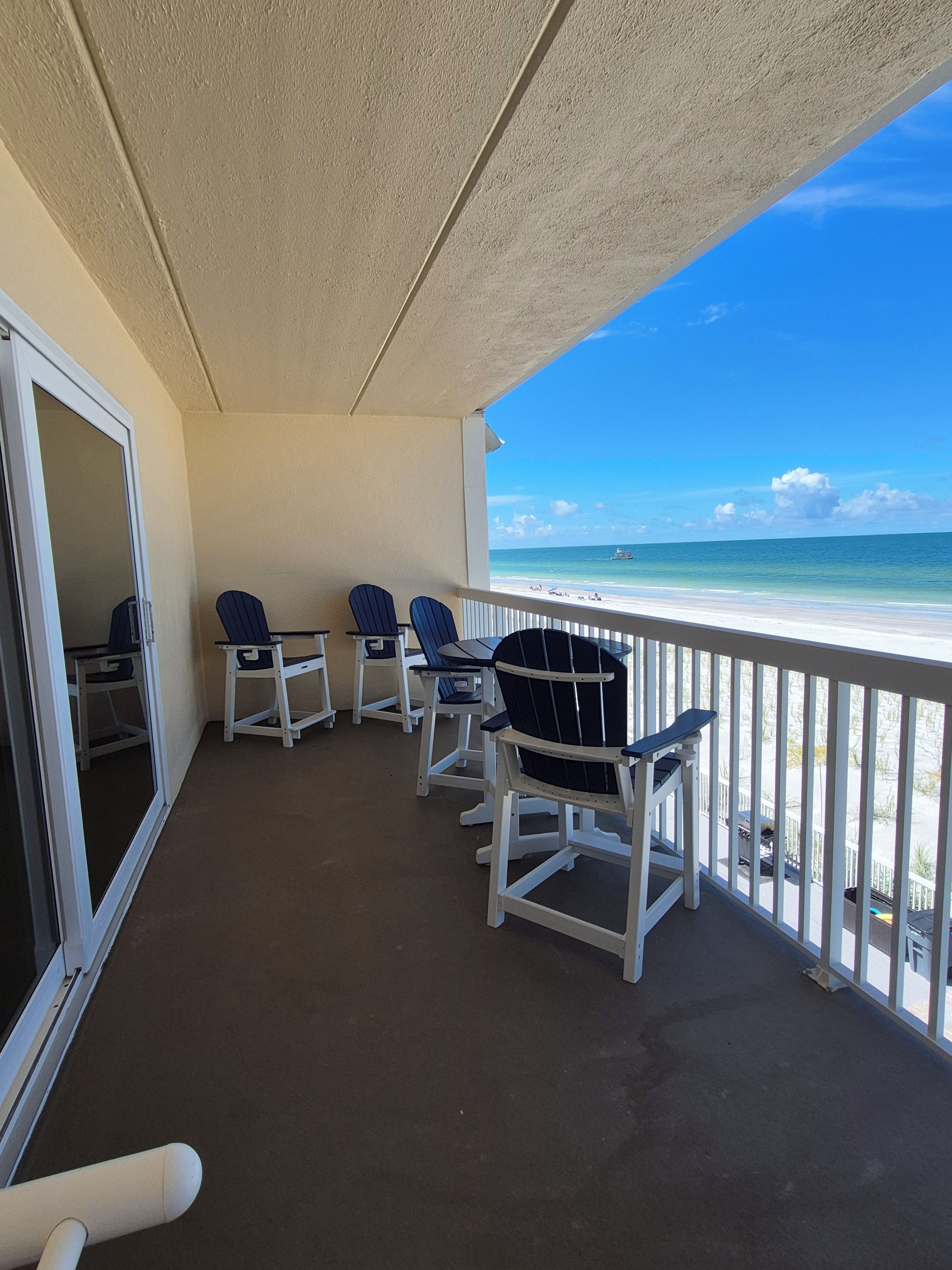 Un balcon avec vue sur la plage, agrémenté d’une rangée de fauteuils Adirondack et d’une porte vitrée donnant sur l’intérieur.