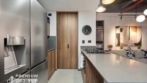 Een moderne keuken met een roestvrijstalen koelkast, houten kasten, een inbouwoven en een groot kookeiland met zitplaatsen.