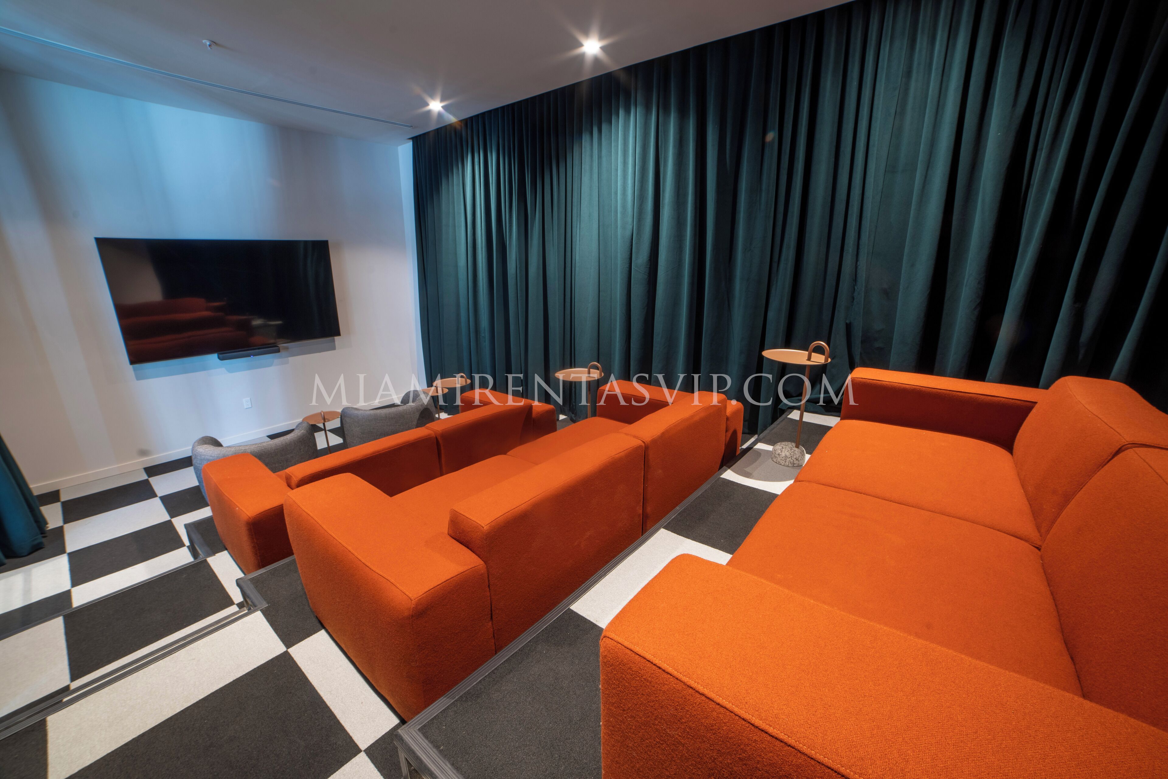 Uma sala de estar moderna com chão xadrez, sofás laranja, televisão de tela plana e uma grande janela com cortinas escuras.