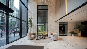 Een moderne lobby met een marmeren vloer, twee banken, een bijzettafeltje en grote ramen met uitzicht op de straat.