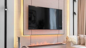 Ein modernes Wohnzimmer mit einem an der Wand montierten Flachbildfernseher, einem integrierten Kamin und einer gemütlichen Sitzecke.
