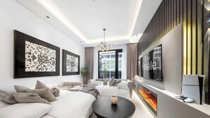 A modern bedroom with a sofa bed, a flat-screen TV, and a fireplace. - Cozy 3BR nr Circle Mall Sleeps 12 | Pool & Sauna (Dubai)