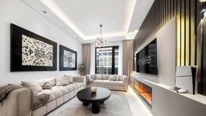A modern living room with a sectional sofa, a round coffee table, and a flat-screen TV mounted on the wall. - Cozy 3BR nr Circle Mall Sleeps 12 | Pool & Sauna (Dubai)