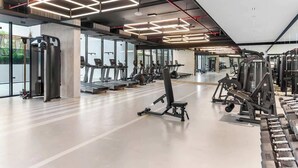 A modern gym with various exercise equipment, large windows, and a clean, spacious layout. - Cozy 3BR nr Circle Mall Sleeps 12 | Pool & Sauna (Dubai)