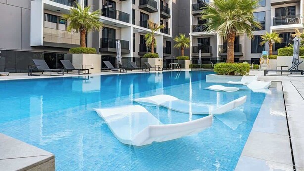 A modern hotel pool area with clear blue water, sun loungers, and palm trees. - Cozy 3BR nr Circle Mall Sleeps 12 | Pool & Sauna (Dubai)