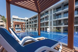 A hotel pool area with multiple lounge chairs and a building with balconies in the background. - Cozy JVC Studio nr Circle Mall by Finelle Living (Dubai)