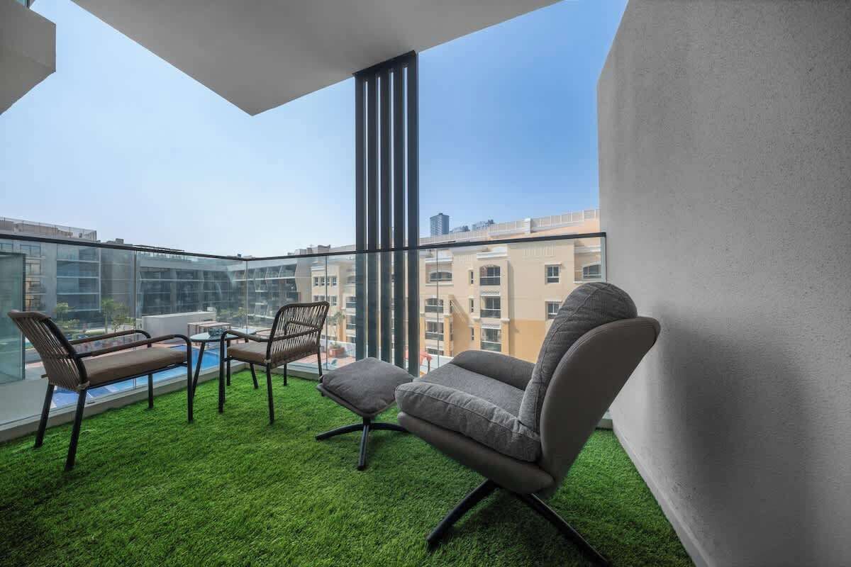 A balcony with a glass railing, a small table, two chairs, and a sofa.
