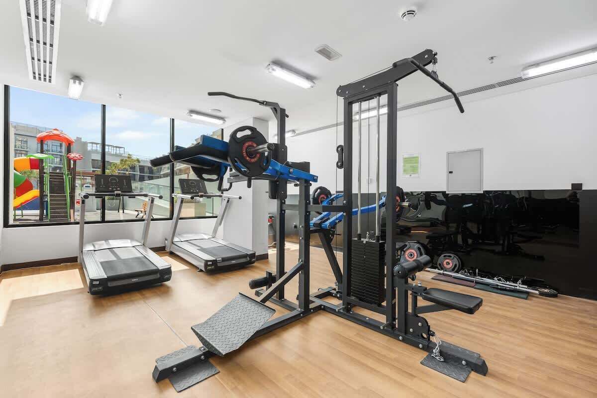 Una palestra con tapis roulant, macchinari per pesi e una piccola area giochi all'aperto visibile dalla finestra.