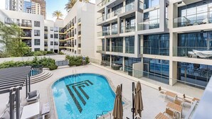 A modern hotel with a rooftop pool, outdoor seating, and a view of the cityscape. - JVC 1BR nr Circle Mall | Sleeps 7 | Pool & Gym (Dubai)