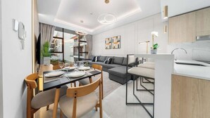 A modern living room with a dining area, a kitchen, and a view of the city. - JVC 1BR nr Circle Mall | Sleeps 7 | Pool & Gym (Dubai)