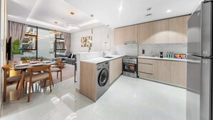 A modern kitchen with a built-in washing machine, a refrigerator, and a dining area with a table and chairs. - JVC 1BR nr Circle Mall | Sleeps 7 | Pool & Gym (Dubai)