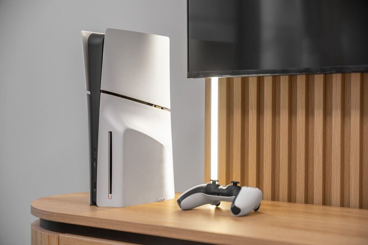 Una configuració de joc moderna amb una consola de joc blanca, un televisor fixat a la paret i un comandament de joc sobre una superfície de fusta.