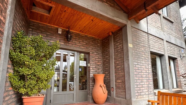 A building entrance with a wooden ceiling, a large potted plant, a large vase, and a bench. - Hosteria Andina (Esquel)