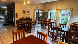 A spacious dining area with wooden tables and chairs, a fire extinguisher on the wall, and large windows allowing natural light. - Hosteria Andina (Esquel)