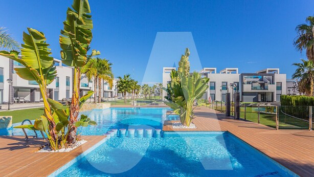 A swimming pool with a wooden deck, surrounded by modern buildings and tropical plants. - Casa Marina in Guardamar (Guardamar del Segura)