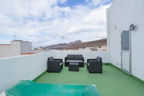 Eine Dachterrasse mit Gartenmöbeln, einer Tür und Blick auf Berge.