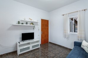 Ein Wohnzimmer mit Fernseher auf einem weißen Schrank, einem blauen Sofa, einer Holztür und einem Fenster mit Vorhängen.