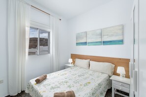 Et soveværelse med en seng, to sengeborde, et vindue med gardiner og tre billeder hængt på væggen.