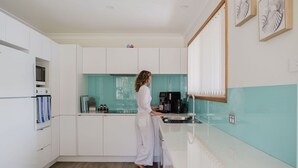 Een moderne keuken met witte kasten, een blauwgroene spatwand en iemand die koffie maakt.