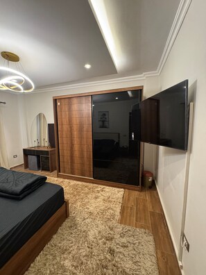 A modern bedroom with a bed, a mirror, a wardrobe, and a television. - Luxury diamond apartment in wesal compound (Cairo Governorate)
