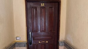 Uma porta de madeira escura com o número 51, uma pequena lixeira e um tapete de entrada.
