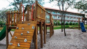 A wooden playground with a slide and climbing structures, set against a building with a red roof. - Hotel Canariu's Gravatá (Gravatá)